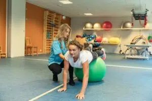 Женщина с физиотерапевтом и гимнастическими снарядами в гимнастическом зале лечебного центра курорта Вярска.