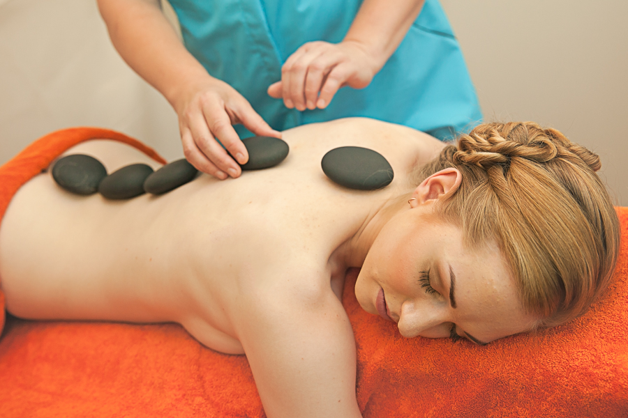 A woman on a massage table with pre-heated stones placed on her back by a masseur. Photo of lava stone massage at Värska spa treatment centre.