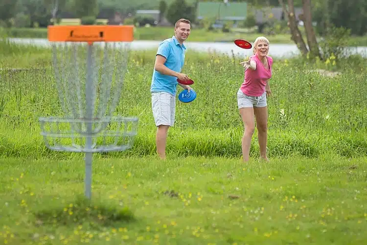 Jaunāks vīrietis un sieviete spēlē disku golfu Vērskas sanatorijas pludmalē.