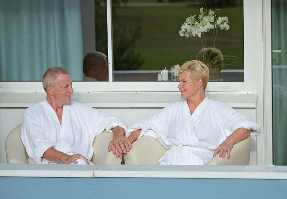 Vīrietis un sieviete baltos peldmēteļos sēž uz Värska sanatorijas viesnīcas balkona.