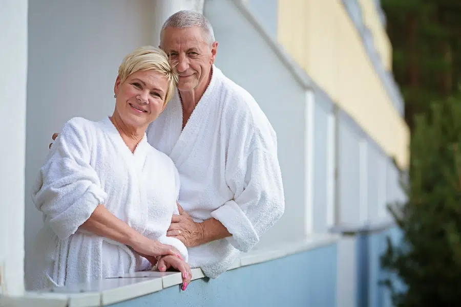 Senioru pāris baltos peldmēteļos uz Värska sanatorijas viesnīcas balkona.