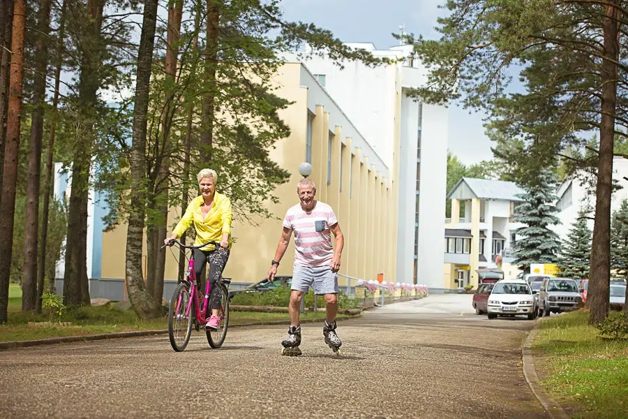 Naine sõidab jalgrattaga ja mees rullusikudega kergliiklusteel Värska kuurrotravikeskuse juures.